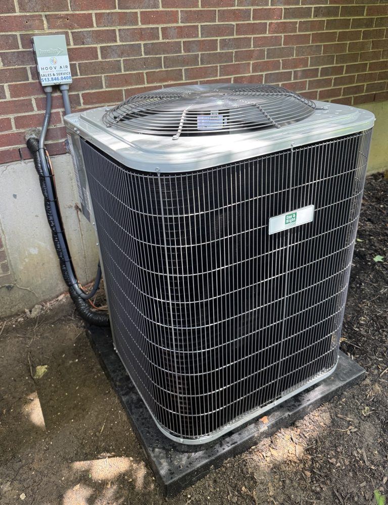 New Day & Night air conditioner condenser installed on a pad beside a brick home