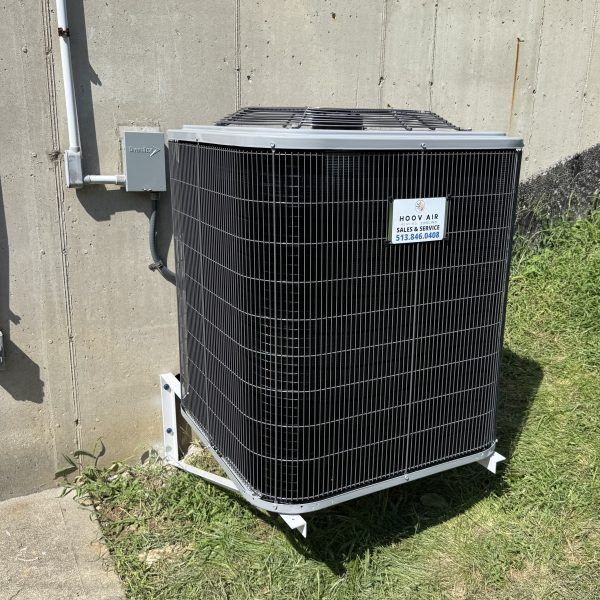 New air conditioner condenser mounted on a stand beside a concrete foundation wall