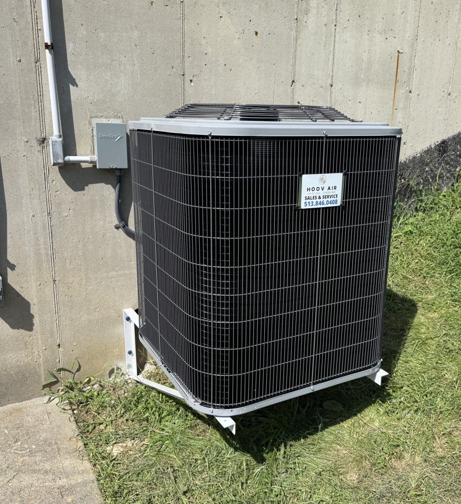 New air conditioner condenser mounted on a stand beside a concrete foundation wall